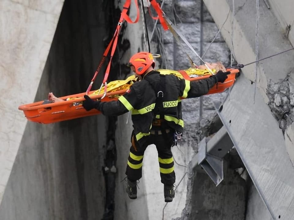 Ein Retter wird durch eine Trümmerspalte der Brücke an einem Seil hochgezogen – und mit ihm eine Person auf der Bahre.