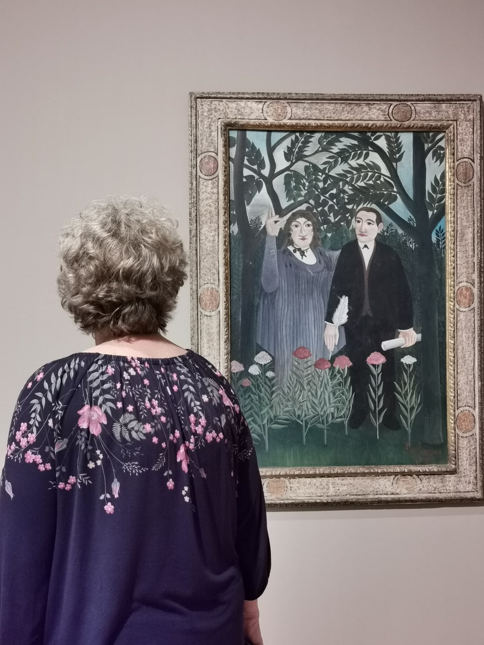 Frau mit Blumenshirt steht vor einem Gemälde im Museum 