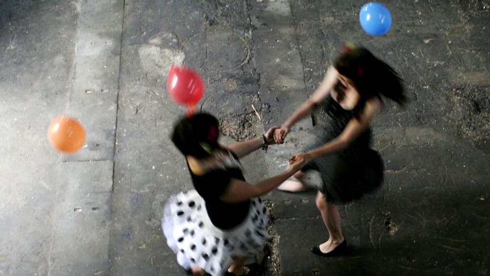 Zwei Frauen, die miteinander tanzen. Luftballons schweben in der Luft.