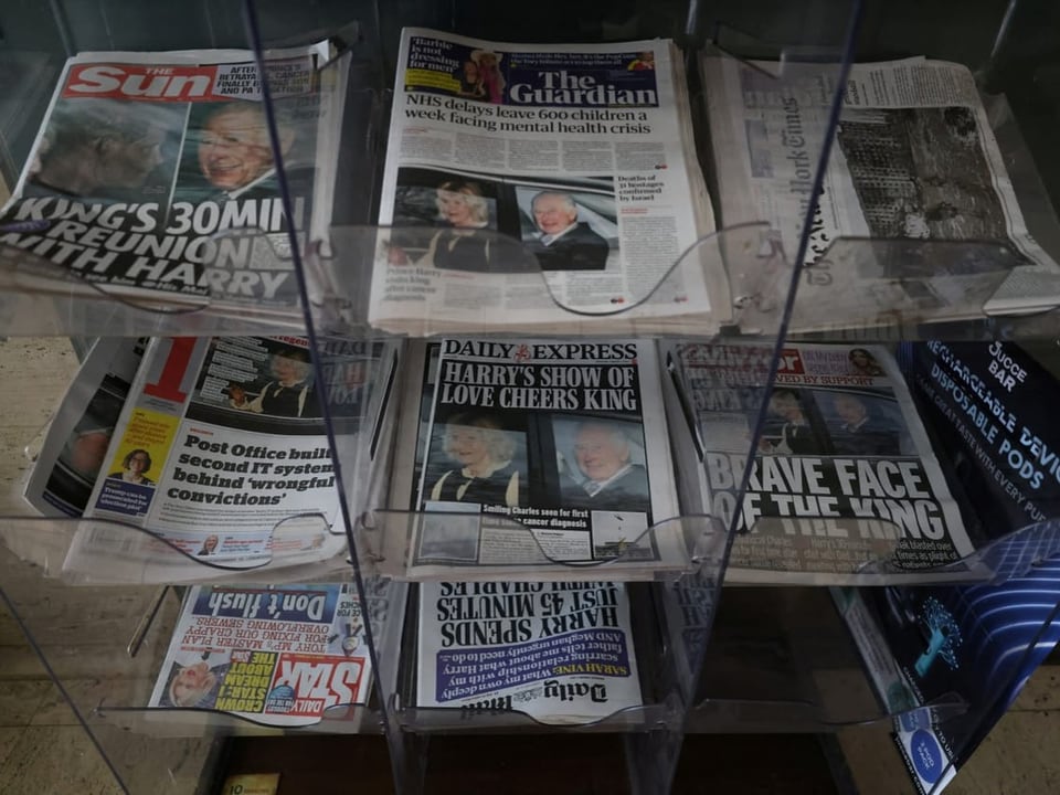 Verschiedene Zeitungen liegen in einem Regal auf. Alle haben die News selbe News auf der Titelseite.