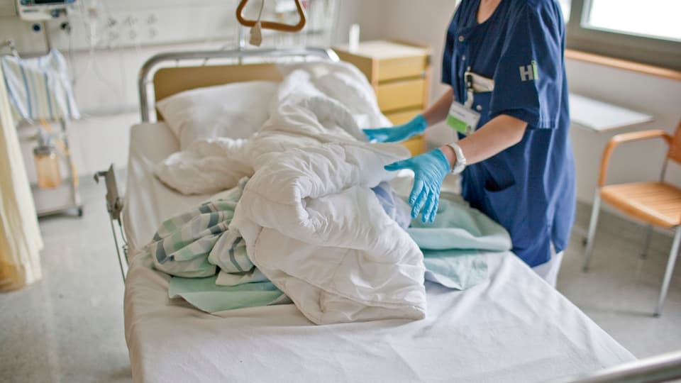 Eine Spitalangestellte räumt ein leeren Spitalbett auf.