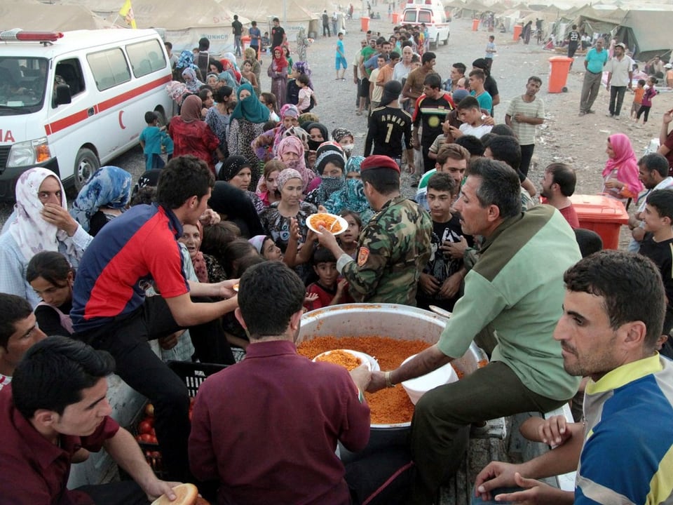 Zahlreiche Flüchtlinge drängen sich um einen Topf mit Essen.
