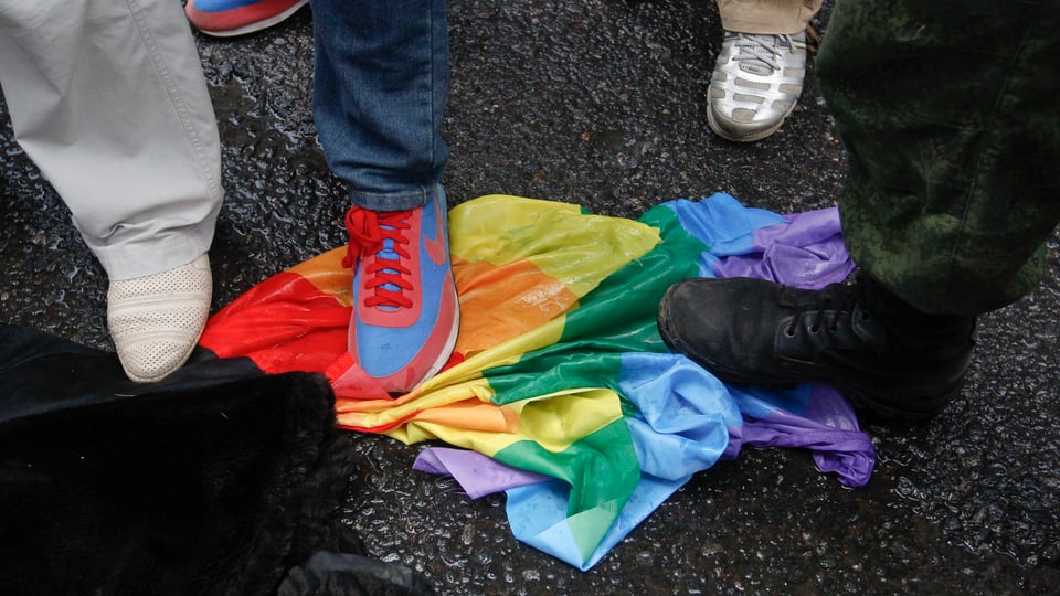 Eine Regenbogen-Flagge wird am Boden zertreten.