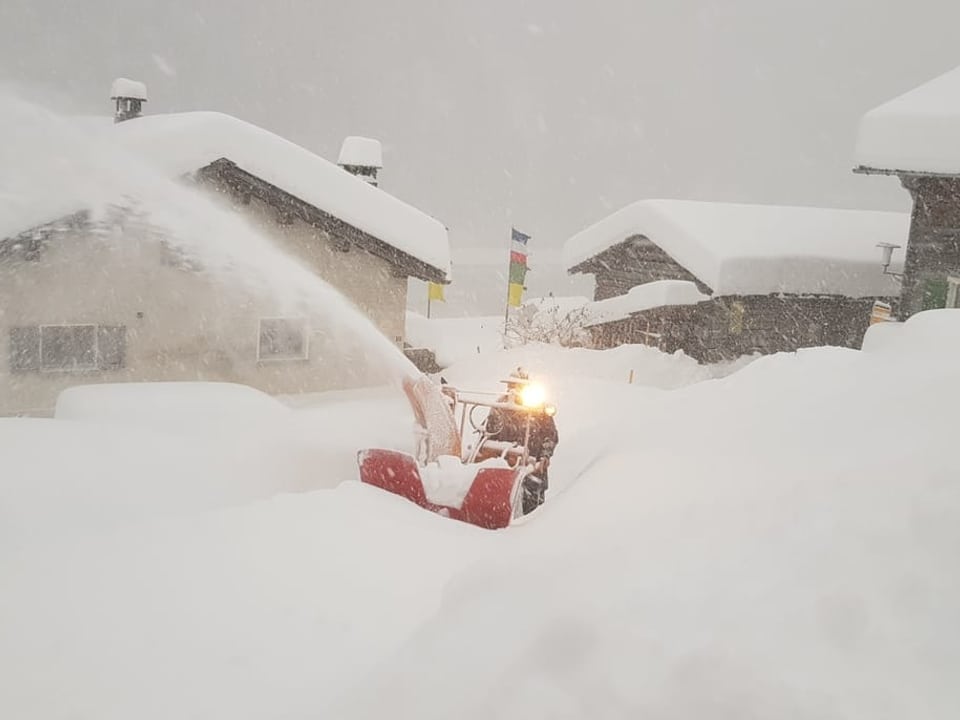 Ein Schneepflug arbeitet sich durch ein verschneites Dorf.