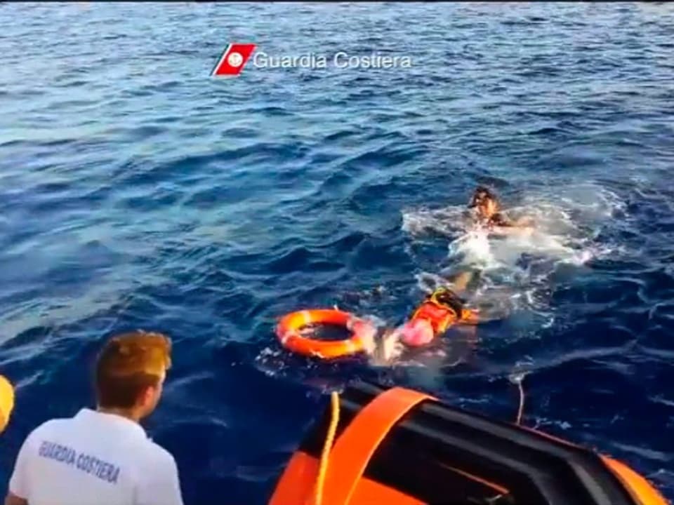 Videoaufnahme von Rettungskräften, die zwei im WAsser treibende Personen zu Rettungsboot ziehen