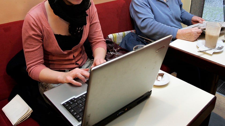 Eine junge Frau sitzt im Café am Laptop.