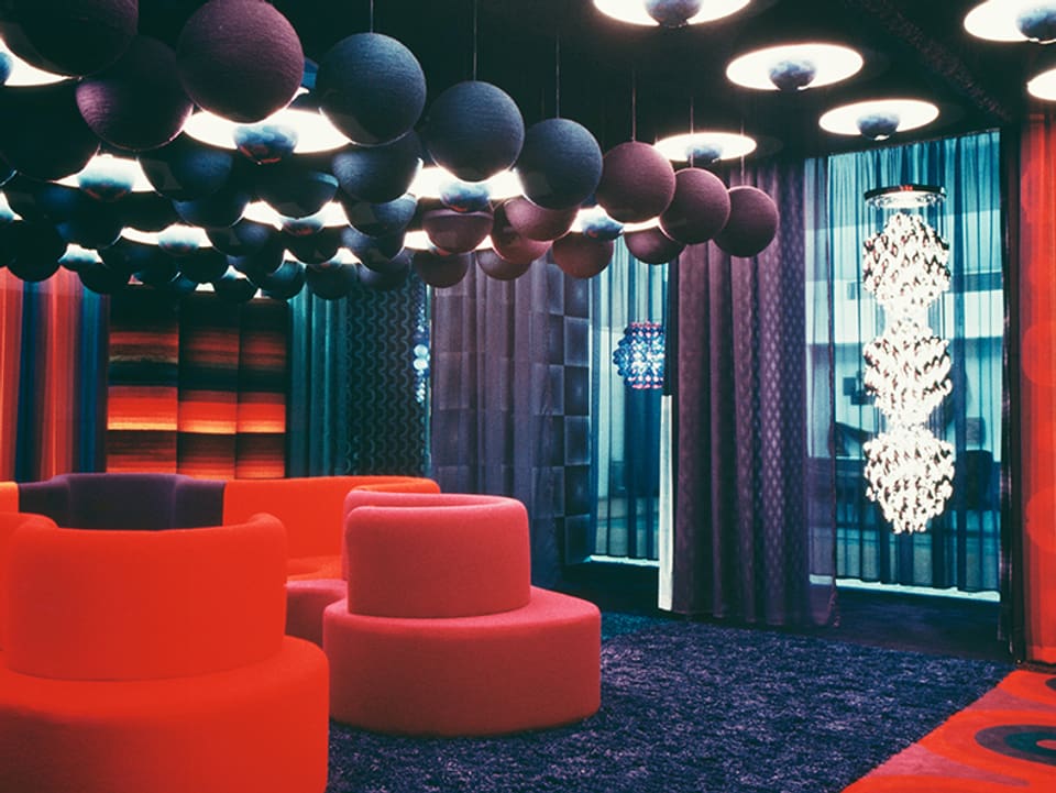 Rote Sitzgelgenehiten in Raum mit blauen und violetten Vorhängen udn blauen und violetten Kugeln an der Decke