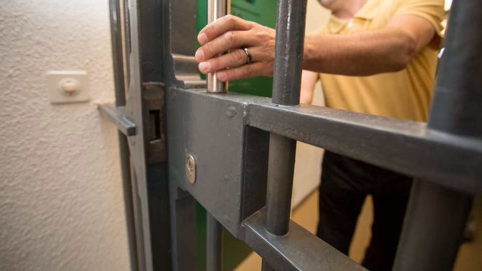 Ein Mann öffnet eine Gittertüre in einem Gefängnis.