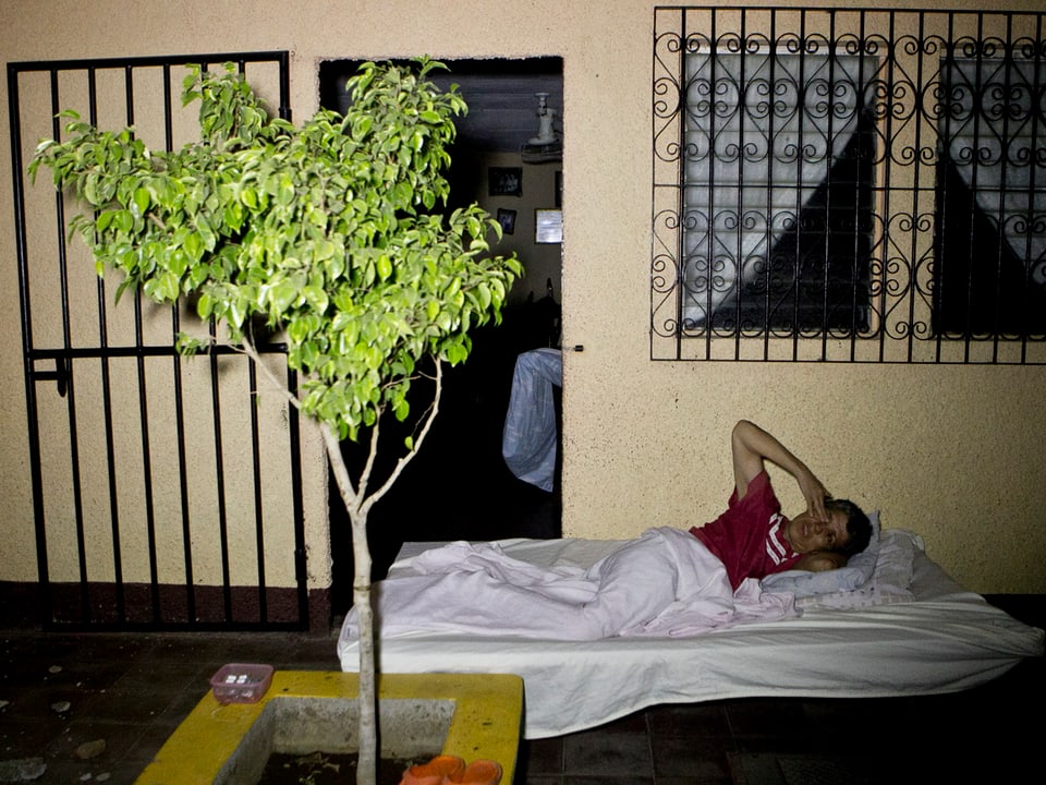 Eine Person liegt nachts vor dem Haus auf einer Matratze am Boden, zugedeckt mit einer weissen Decke.