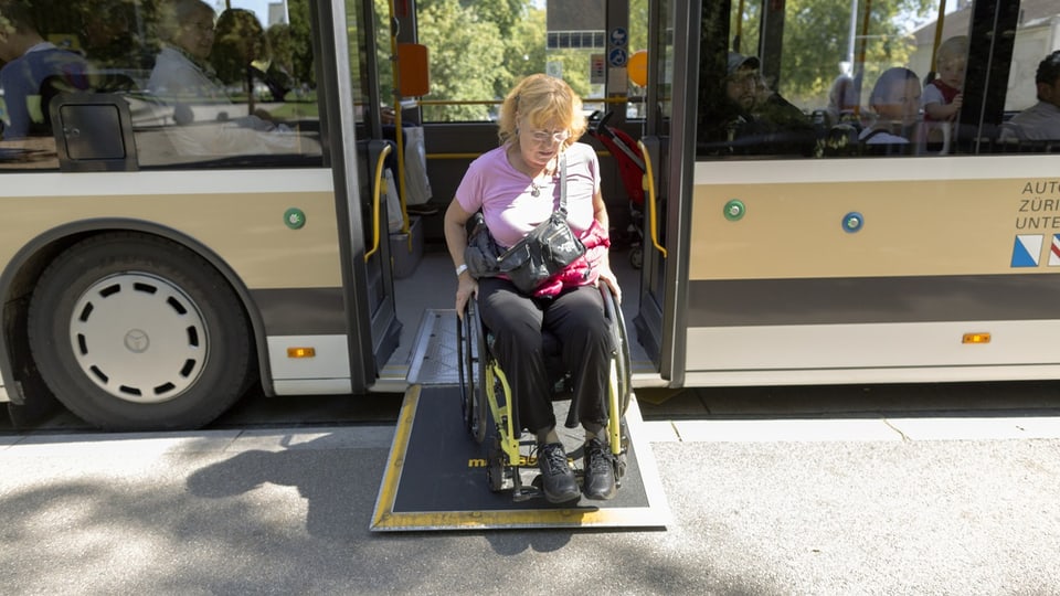 Eine Frau in einem Rollstuhl fährt aus einem Bus heraus.