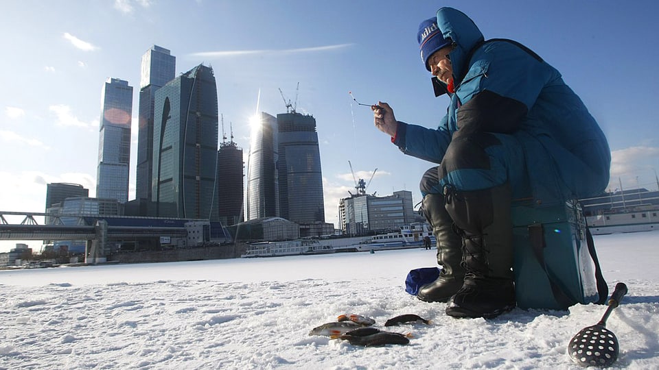 Ein Mann der auf einer Eisfläche Fische fängt.