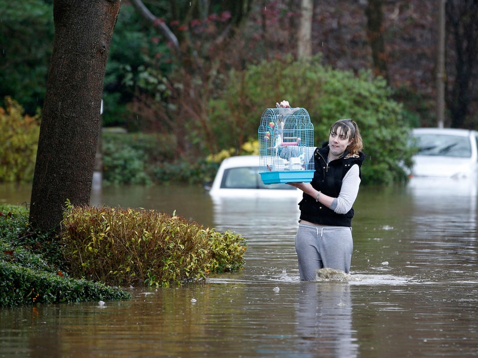 Eine Frau trägt einen Vogelkäfig durch eine überflutete Strasse.