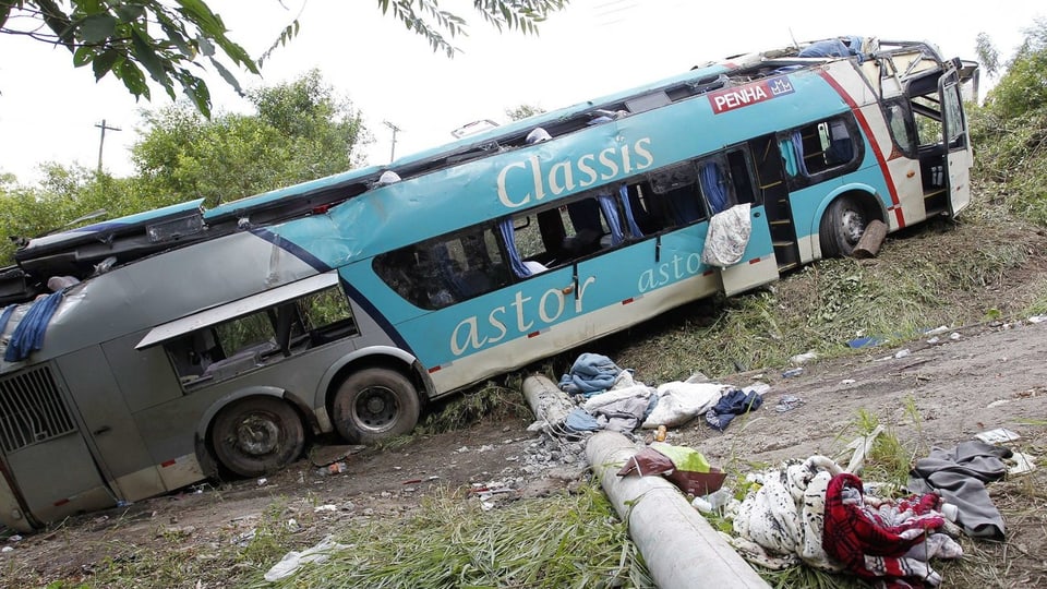 Ein Bus liegt in einem Abhang, teilweise sind Fenster zerbrochen und Kleider liegen herum.