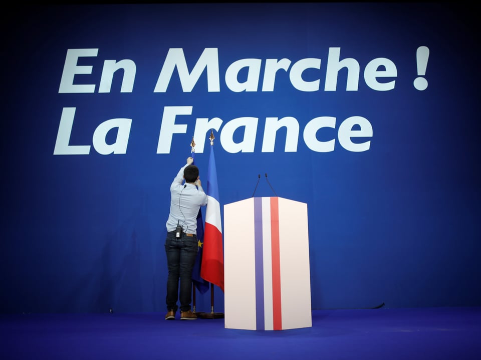 En Marche! Schriftzug vor Rednerpult und französischer Flagge. 