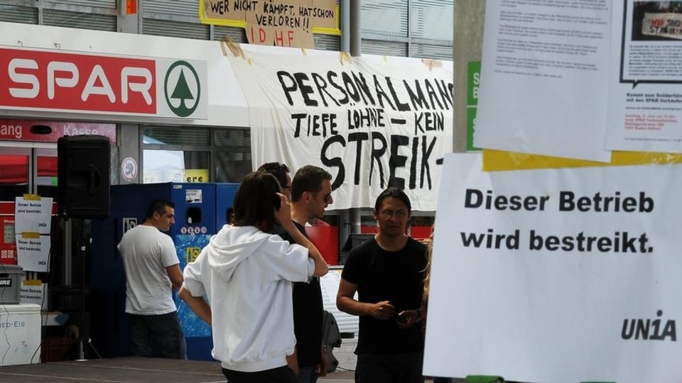 Männer stehen vor dem Tankstellen-Shop in Dättwil. Am Shop hängen Plakate mit Streik-Parolen.