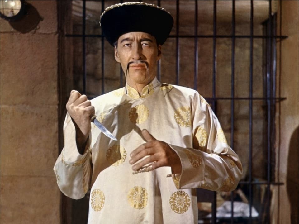 Lee als Fu Manchu mit einem asiatischen Umhang, Hut und langem Schnauz. In der Hand hält er ein Messer.