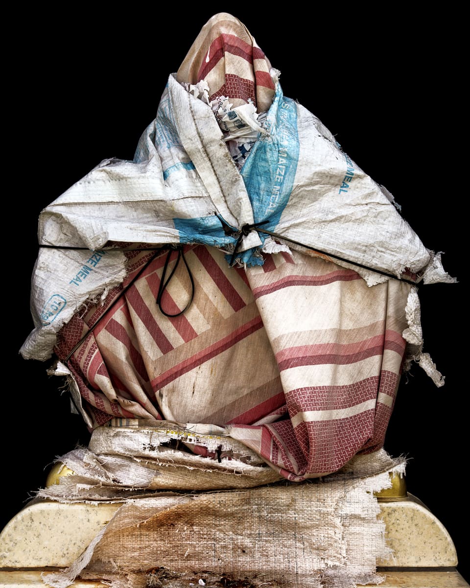 Ein dreieckiger Gegenstand, der mit mehreren farbigen Tüchern umwickelt und mit Schnur zsuammengebunden ist.