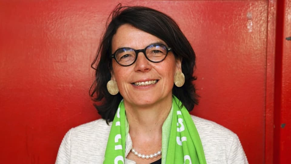 Eine Frau mit Brille und grünem Schal vor roter Wand.