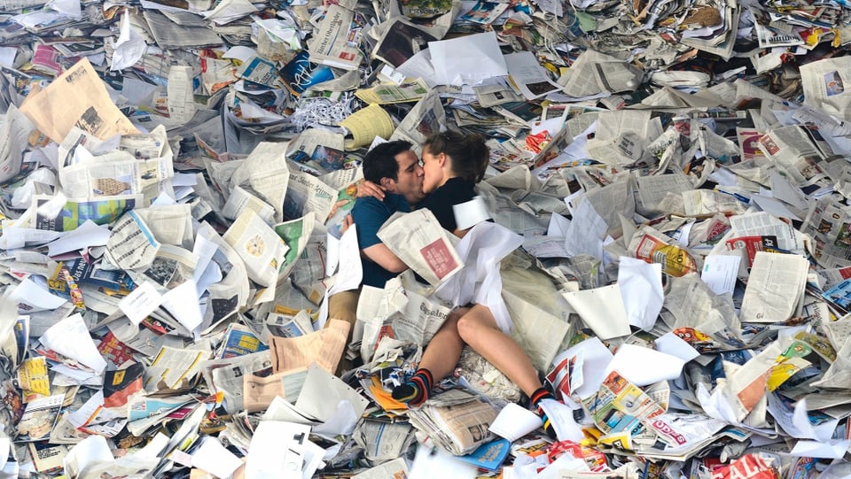 Das Filmliebespaar küsst sich unter lauter Altpapier.