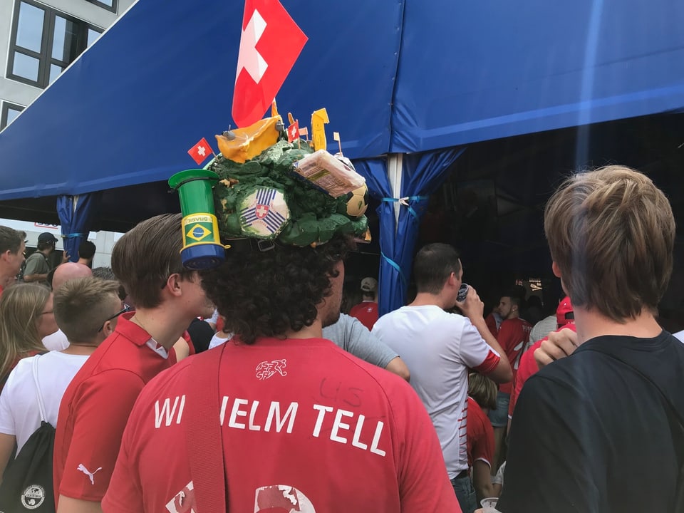 Ein Fussballfan mit einem speziell auffälligen Hut mit Schweizerkreuz, Käse und Brasilienfahne
