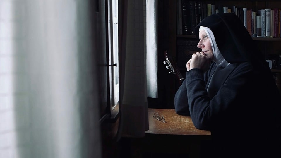 Eine Nonne sitzt an einem Tisch und schaut durchs Fenster