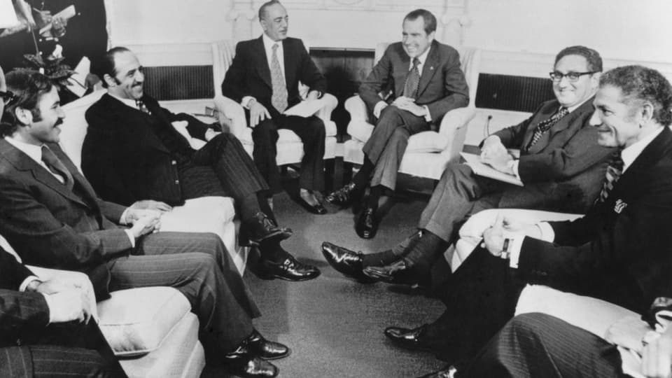Schwarz-weiss-Foto: Die Politiker sitzen in einem Halbkreis auf Sofastühlen zusammen.