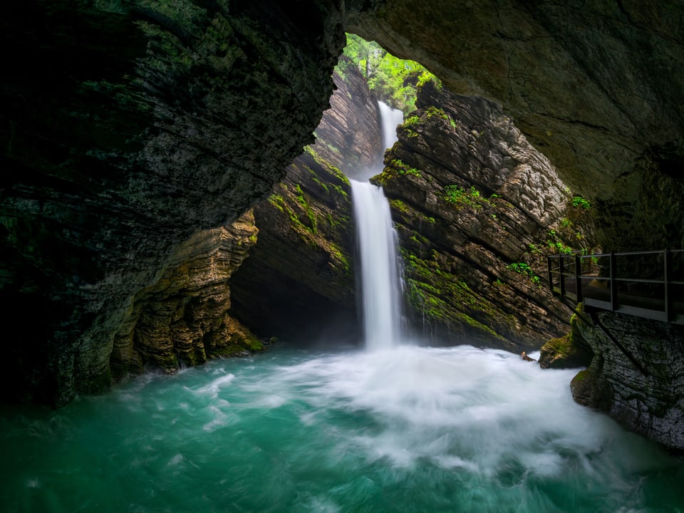 Eine kleiner Wasserfall stürzt über einen Felsvorsprung. Der Fotograf steht in einer Höhle.