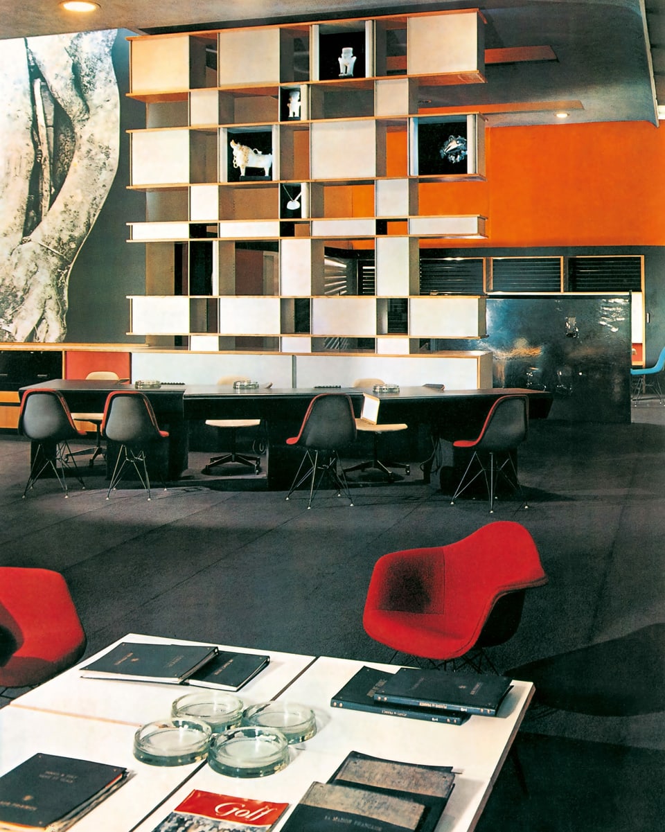 Empfangsbereich der Büros von Air France in London, um 1960. Ein weisses Rregal, im Vordergrund sind zwei rote Eams-Stühle.