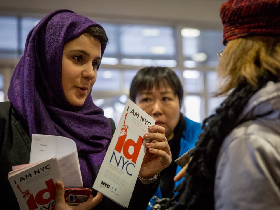 Eine Frau mit Kopftuch verteilt Broschüren mit der Aufschrift "IDNYC"