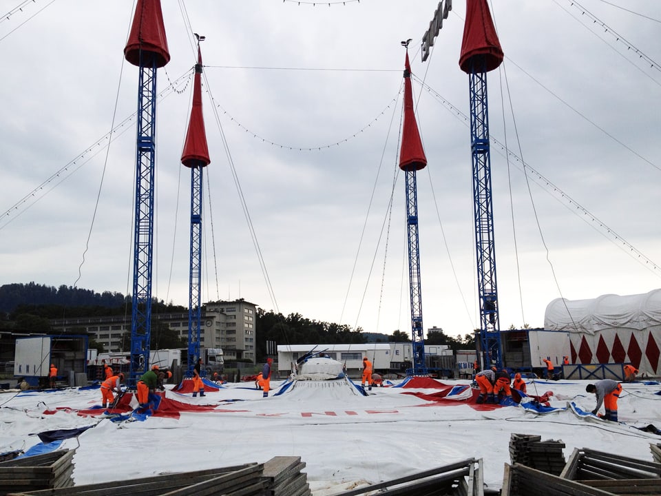 Arbeiter in orangen Gewändern bauen das Zelt des Zirkus Knie auf.