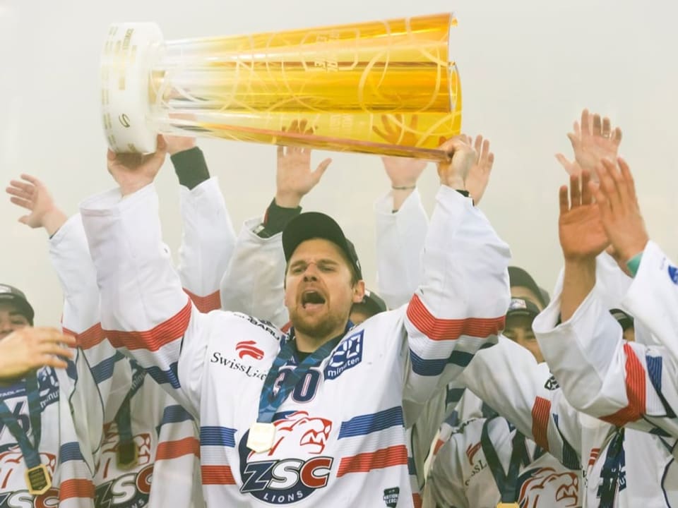 Lukas Flüeler stemmt den Meisterpokal in die Höhe.