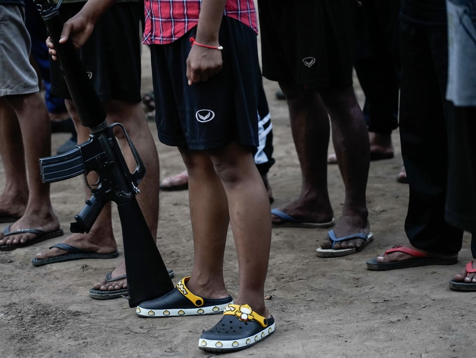 Die Beine von Guerilla-Kämpfern sind zu sehen, einer hält eine Waffe