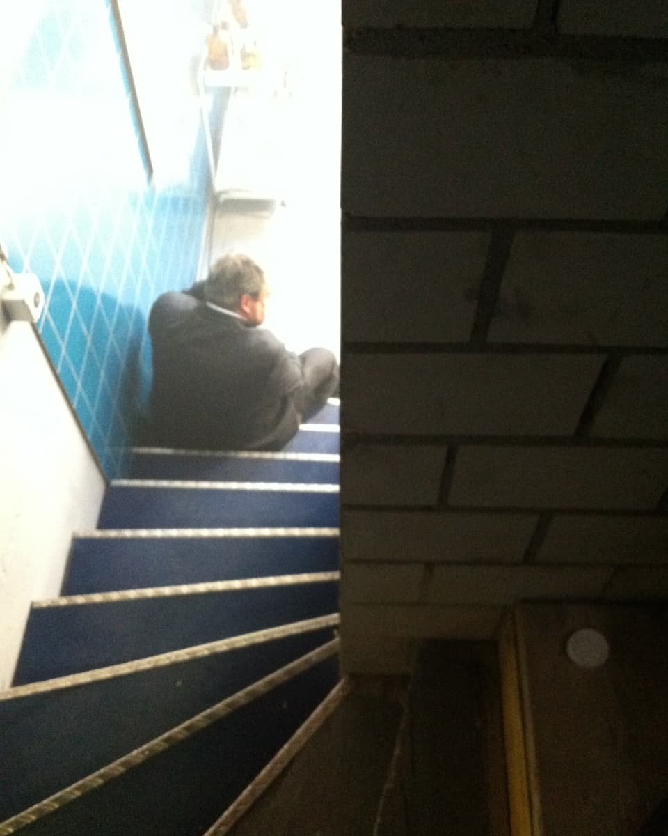 Aufnahme von oben auf eine Treppe. Unten sitzt Mike Müller auf einer Stufe.