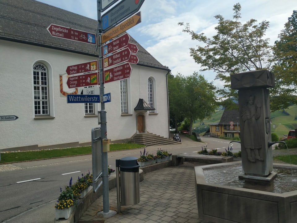 Dorfbrunnen und Wegweiser in alle Richtungen für Auto- und Velofahrer.