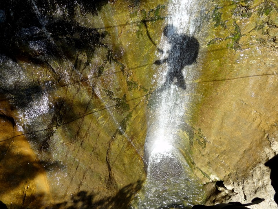 Der Schatten einer Person auf einer Seilbrücke fällt auf den dahinterliegenden Wasserfall.