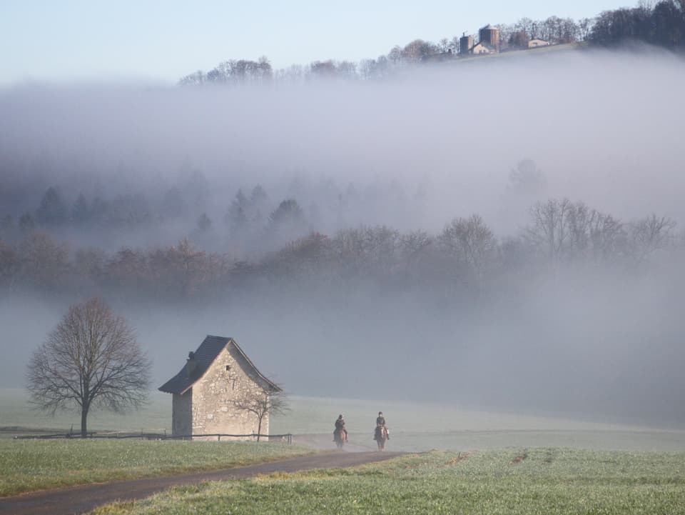 Grenze zwischen Nebel und Sonnenschein. Im Vordergrund zwei Reiter.
