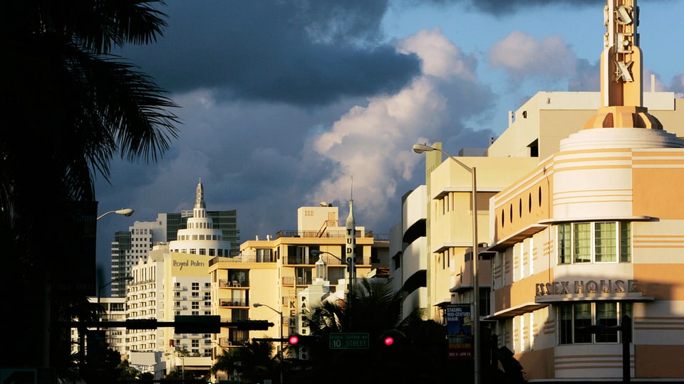 Art Deco Häuser von Miami werden durch durch die Abendsonne beschienen, dahinter türmen sich dunkle Wolken auf. 