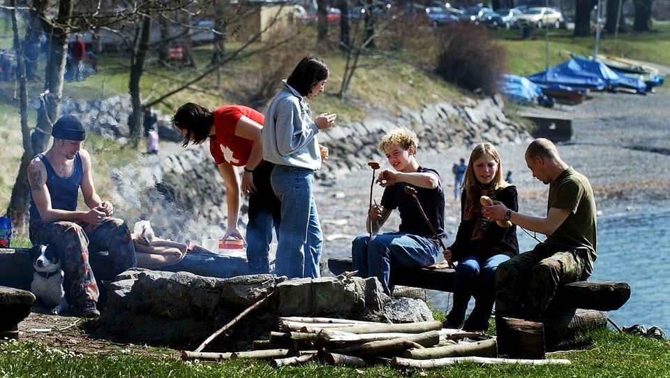 Junge Leute sitzen um eine Feuerstelle und grillieren.