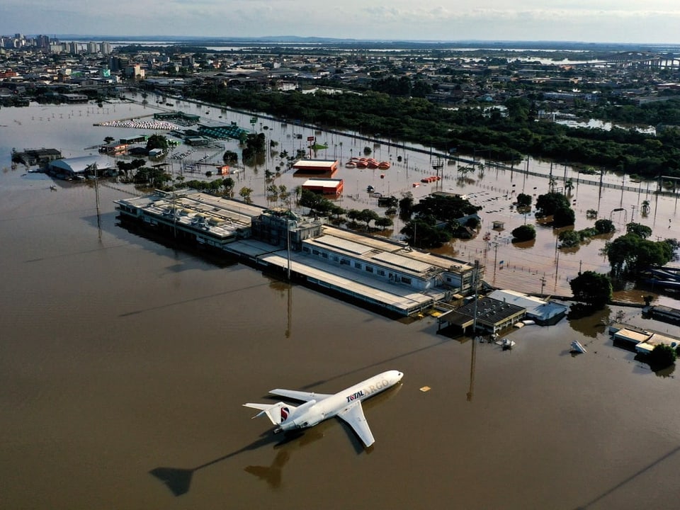 Blick auf ein Flughafengebäude mit einem Flugzeug davor. Beide sind von braunem Hochwasser umgeben. Alles ist überflutet
