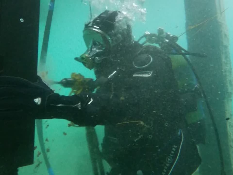 Taucher arbeitet unter Wasser an einem Pfosten.