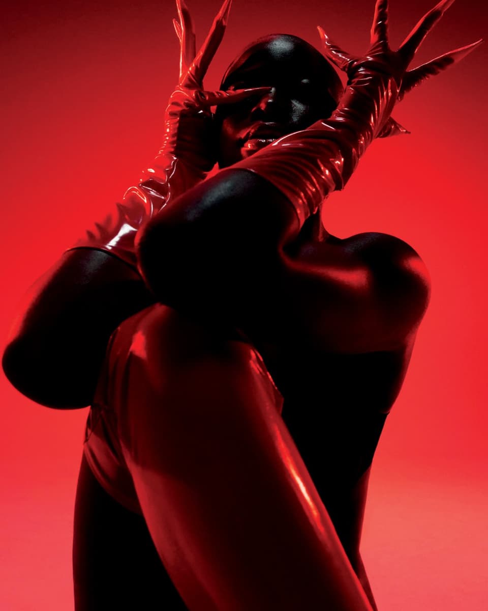 Schwarze Frau vor rotem Hintergrund mit roten Lackhandschuhen mit spitzigen Nägeln.