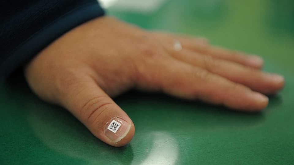 Ein QR-Code ist auf den Fingernagel eines Daumens geklebt.