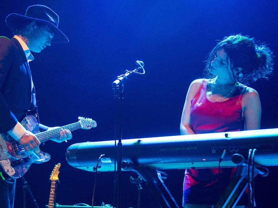 Mann mit Gitarre neben einer Frau am Keyboard auf einer Bühne.