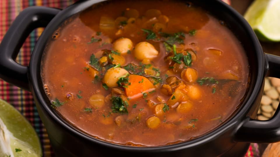 Rot-orange dünne Suppe mit Einlage aus Kichererbsen und Linsen, mit Kräutern garniert