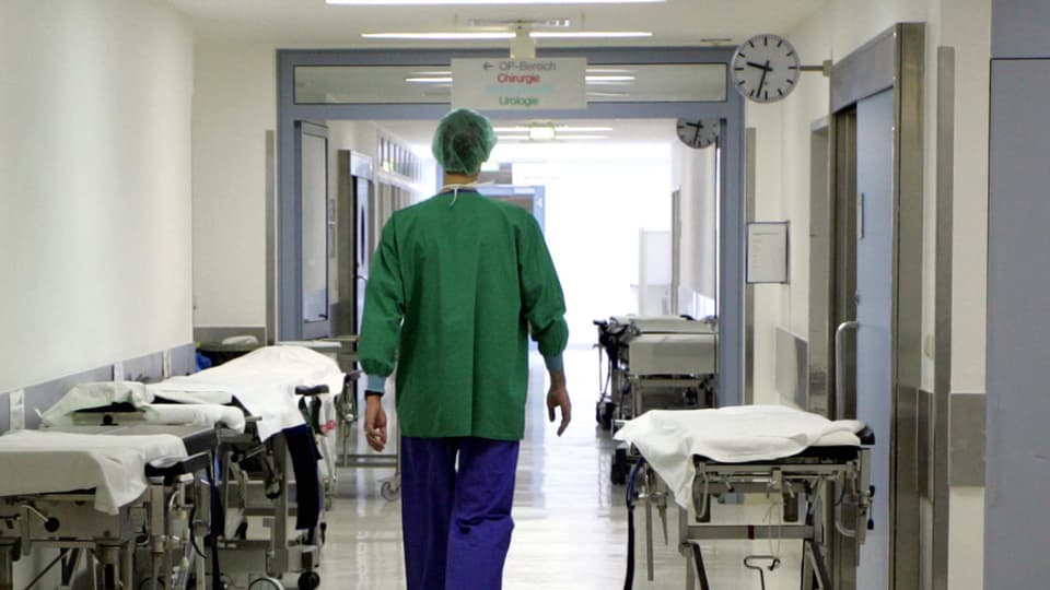 Ein Mann in OP-Klamotten geht einen Spitalgang entlang, links und rechts Bahren.