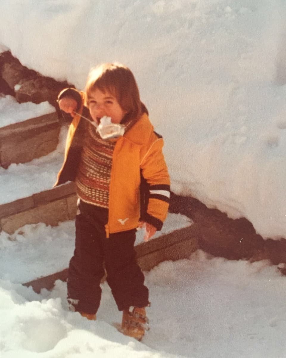 Ein Kleinkind hält einen mit Schnee gefüllten Schöpflöffel vor den Mund.