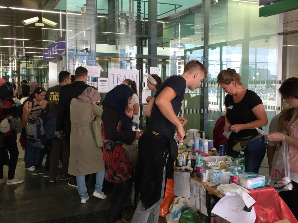 Flüchtlinge stehen vor Tischen mit Spenden