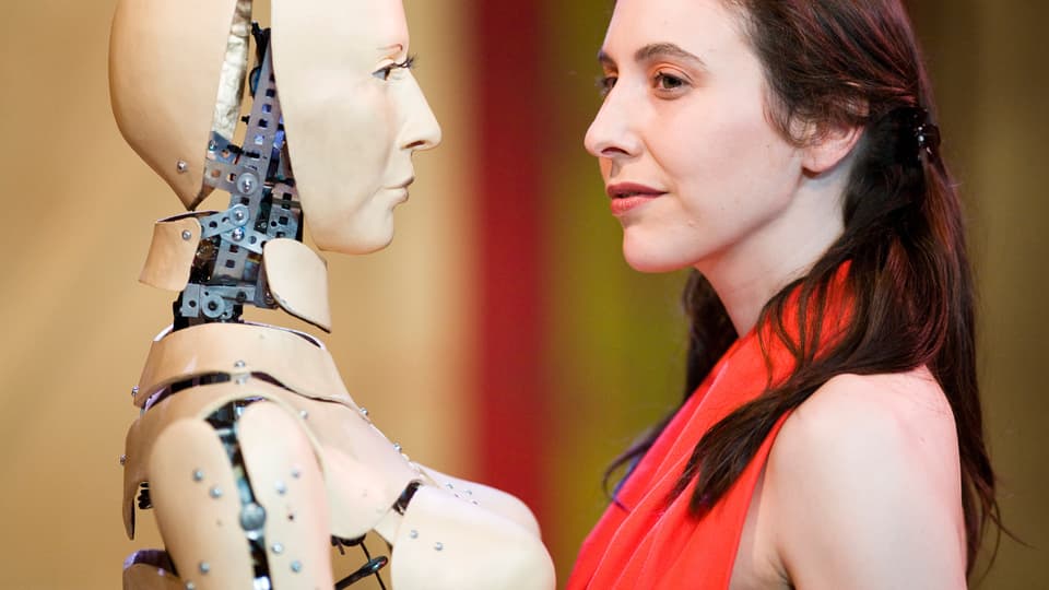 Ein Roboter steht einer Frau in rotem Kleid gegenüber.