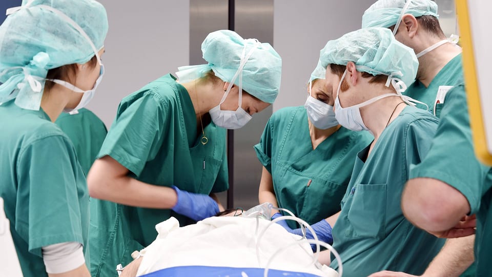 Symbolbild: Mehrere Personen in Operationsgewändern stehen um einen operierten Patienten.