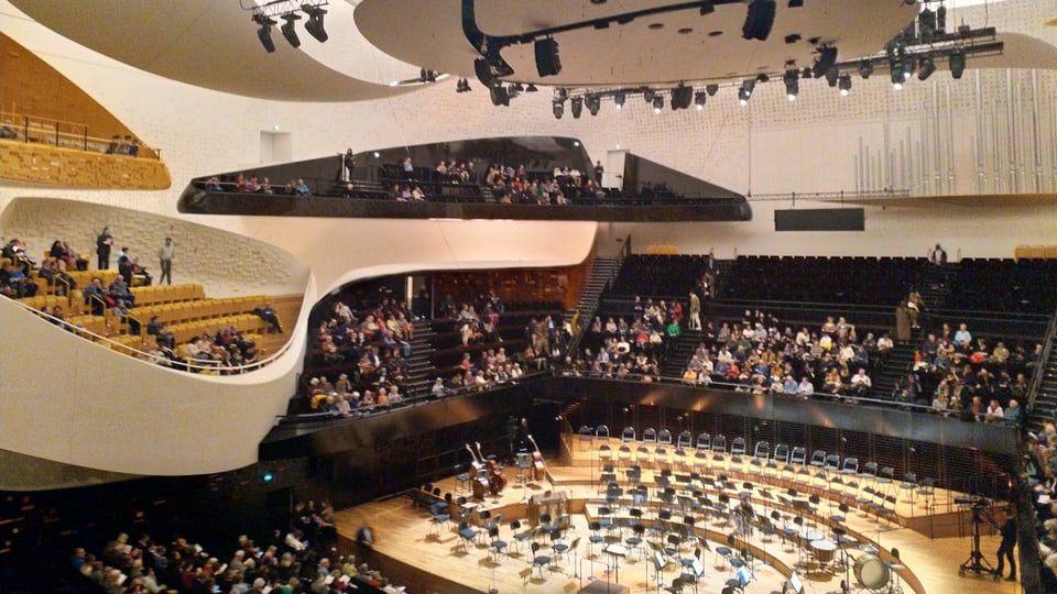 Ein grosser Konzertsaal. Menschen machen sich bereit für eine Aufführung.